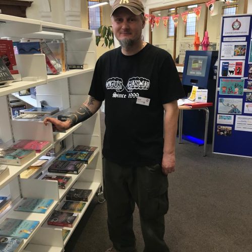 Man in Yankees cap and black t-shirt standing next to book display shelves in library with arched ceiling