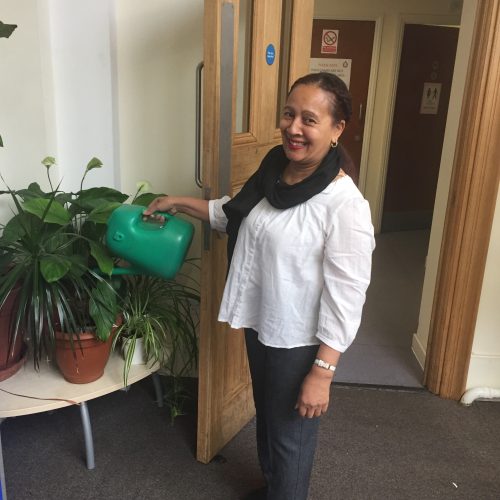 Woman in white shirt watering office plants with green watering can in modern workplace lobby