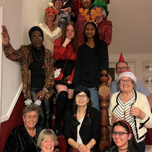 Group of women wearing festive Christmas costumes and accessories posing together on staircase for holiday party