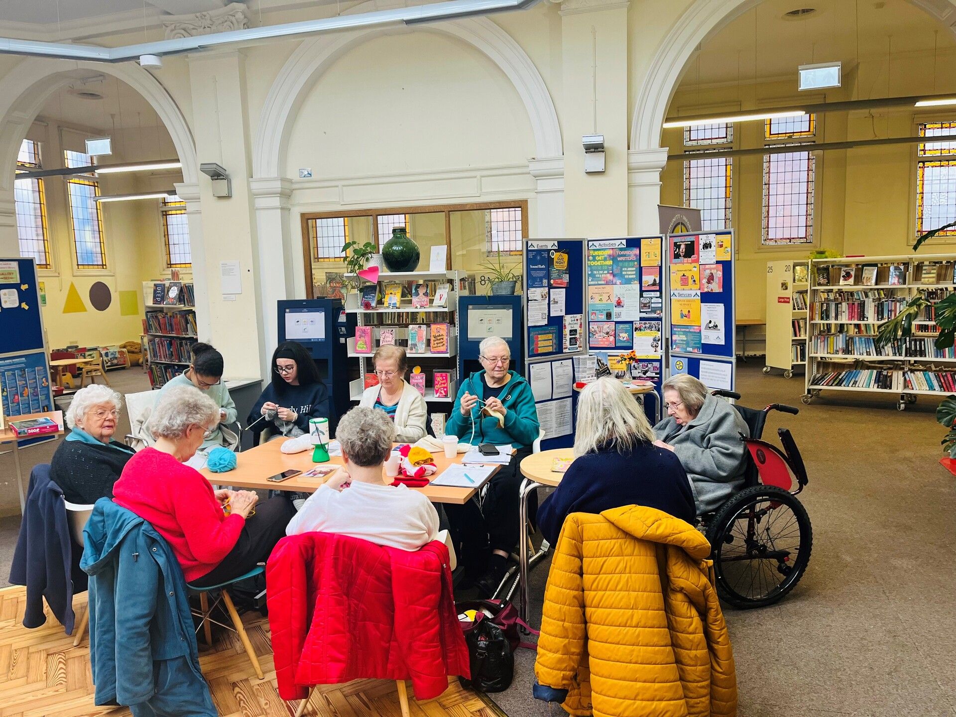 Senior adults participating in craft activities at community table in historic library with arched columns and bookshelves