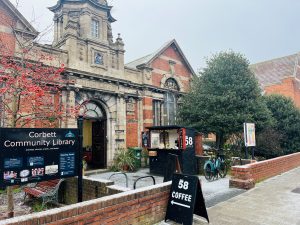 Historic Corbett Community Library building with red brick facade, ornate stone entrance, and coffee shop signage outside