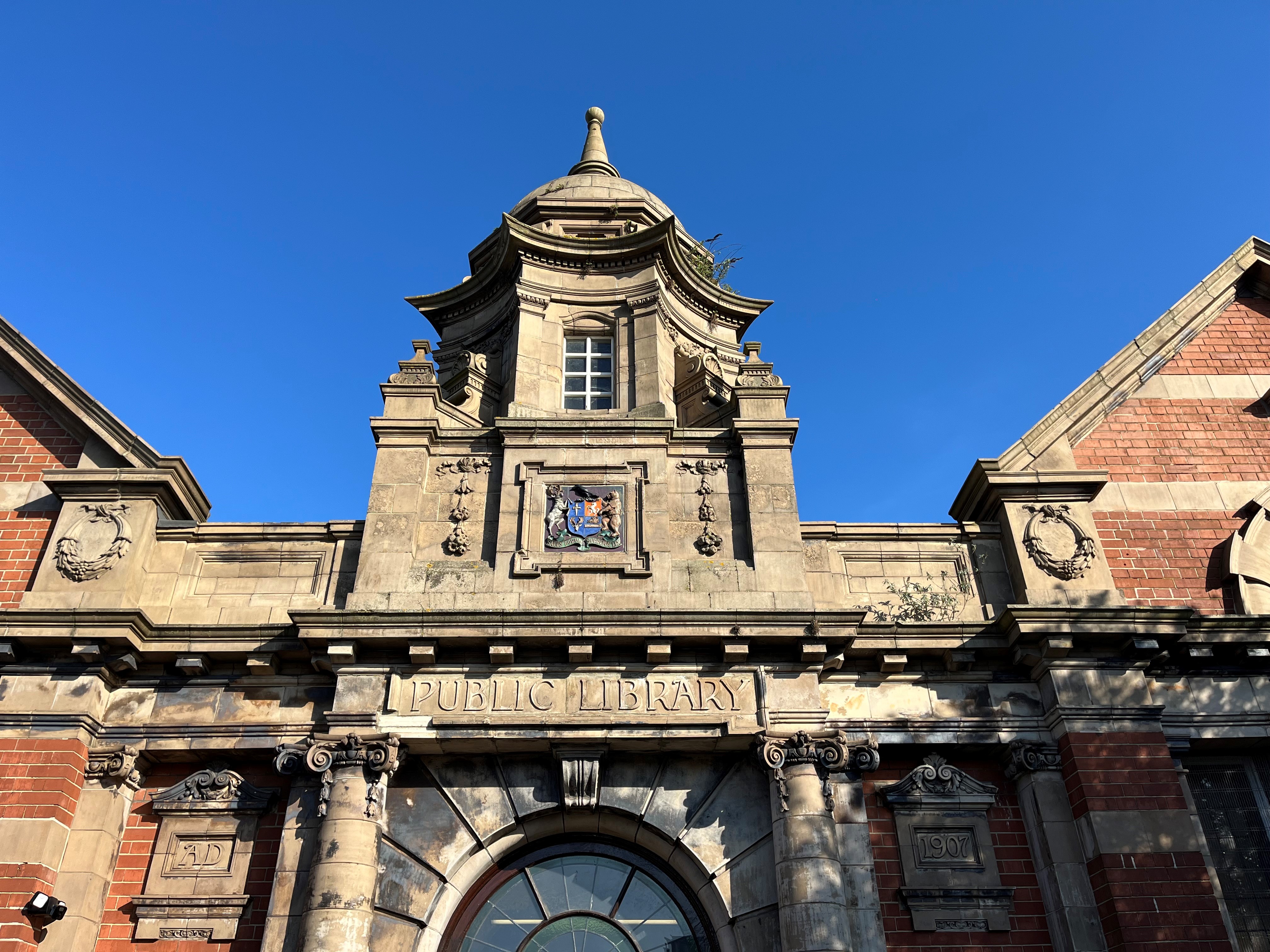 Historic red brick public library building with ornate stone tower and classical architecture against blue sky