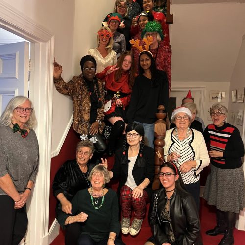 Group of women in festive holiday attire and costumes posing together on staircase at Christmas party celebration