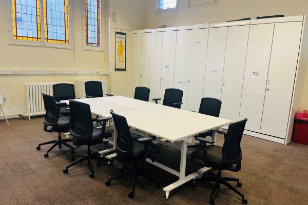Modern conference room with white table, black office chairs, storage lockers and stained glass windows