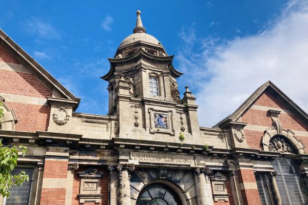 Historic public library building with ornate stone tower, brick facade, and classical architectural details against blue sky.