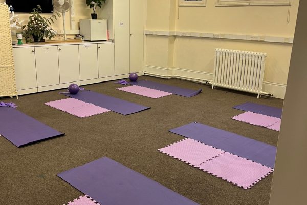 Yoga studio with purple mats and pink foam tiles arranged on carpet floor, featuring stained glass windows and storage.