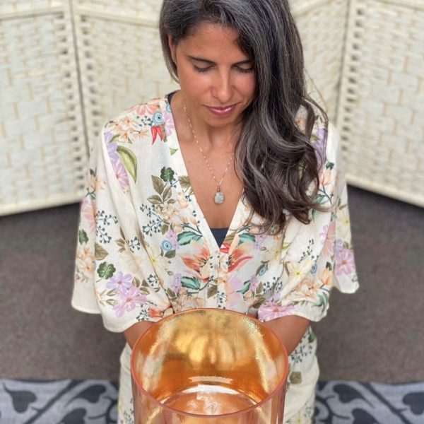 Woman in floral robe holding golden singing bowl for meditation and sound healing therapy session