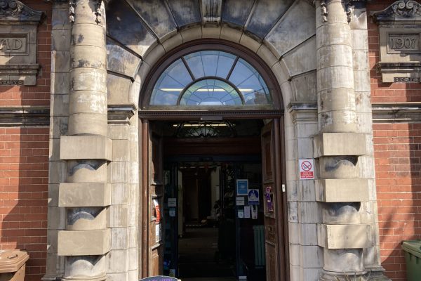 Historic public library entrance with ornate stone columns, arched doorway, and decorative architecture from 1907.