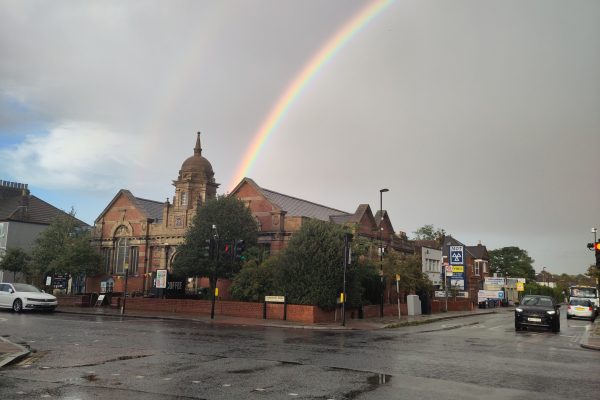 Rainbow over historic red brick church with dome tower on wet street after rain in British town