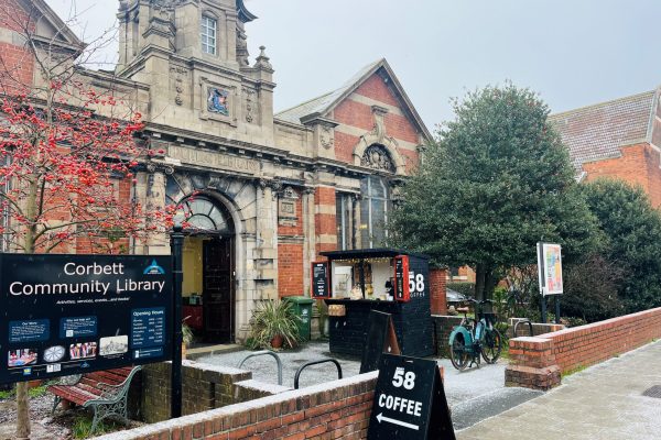 Historic Corbett Community Library building with red brick facade, ornate stone entrance, and coffee shop signage outside